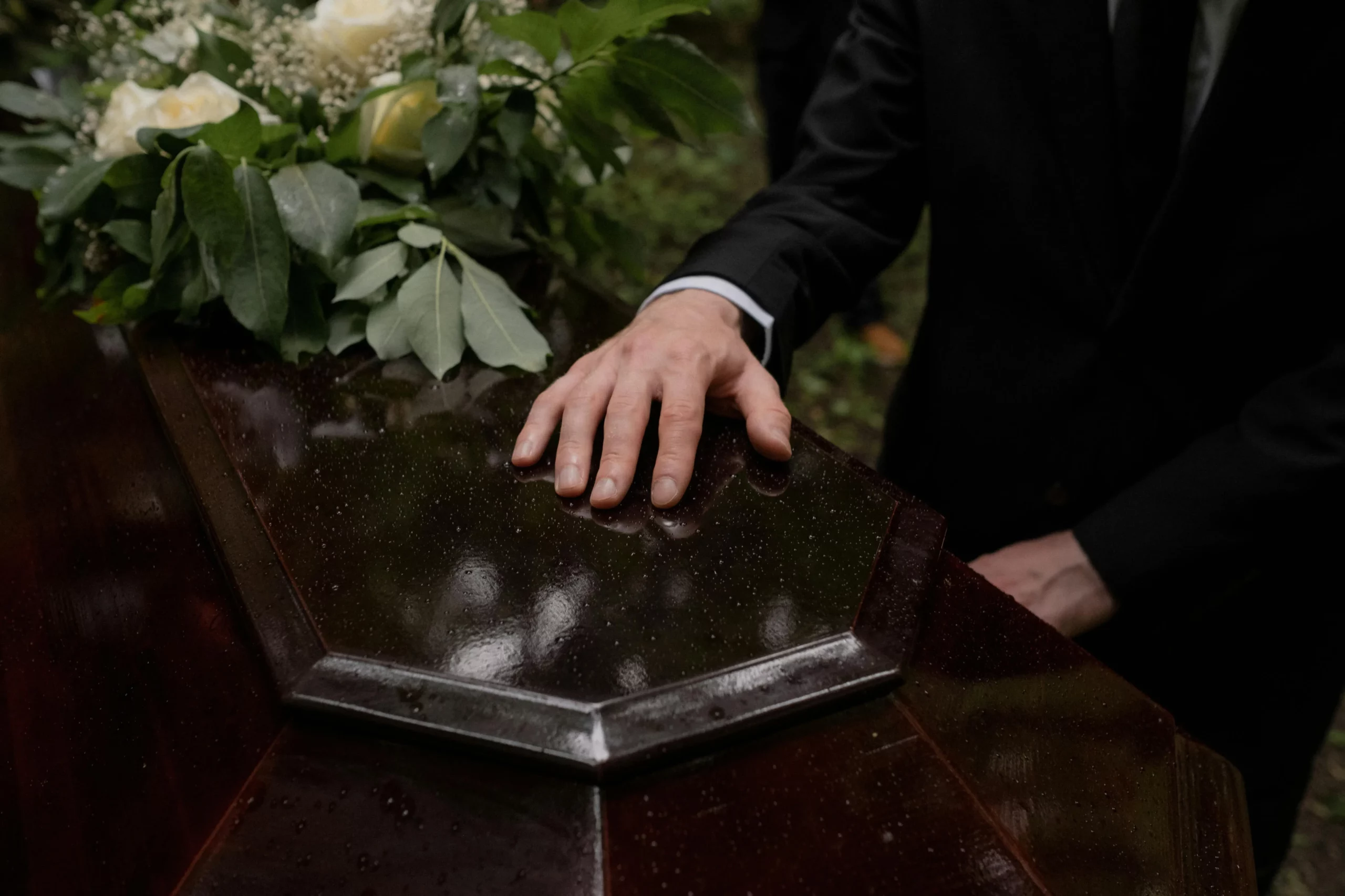 Main posée délicatement sur un cercueil en bois verni sombre.